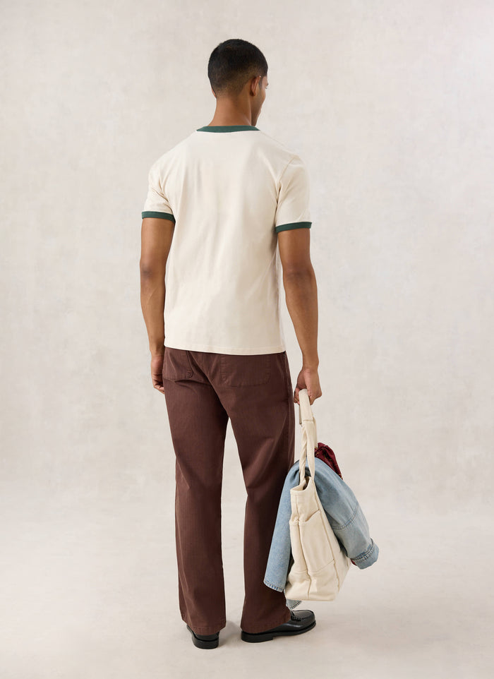 Rear view of a model wearing the cream Guinness x Percival ringer T-shirt with forest green trim.