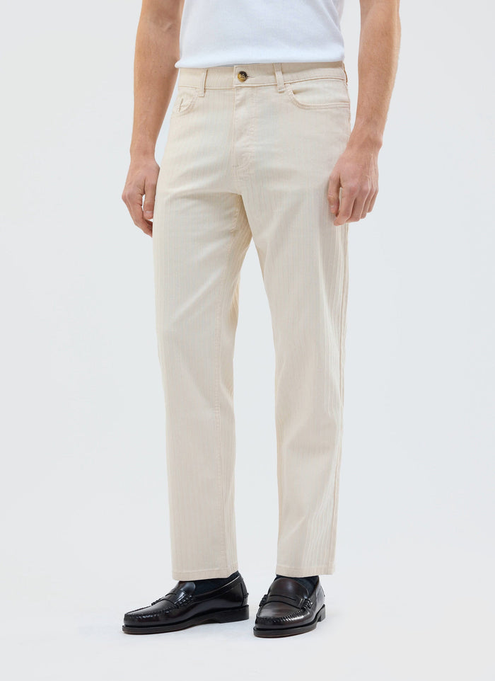 A model wears the Percival Rocco 5 Pocket Trousers in ecru with a white top and black loafers against a white background.