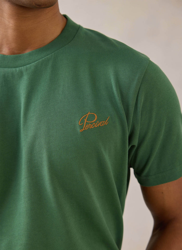 Close-up of a model wearing a forest green organic cotton Percival T-shirt with contrast script chest embroidery.