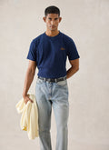 A model wears the navy Percival script embroidered t-shirt, styled with light blue jeans and holding a cream knit.