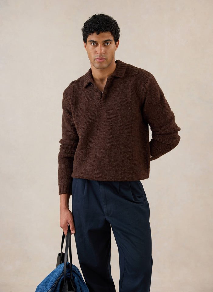 A model wears the brown Percival Shugart Boxy Knit Jumper, styled with dark trousers and holding a bag in a studio.