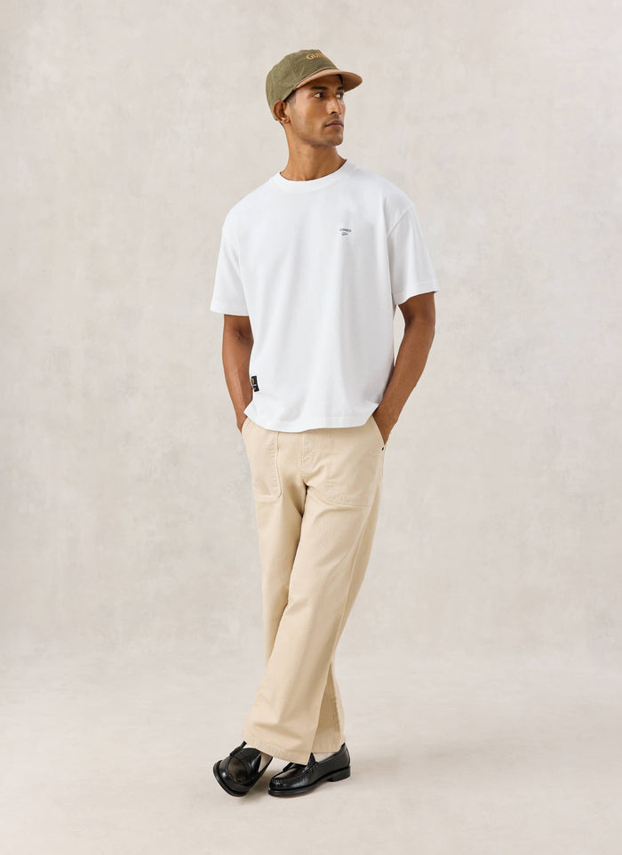 Model wearing the white Soloist oversized T-shirt from Guinness x Percival with beige trousers and a cap.