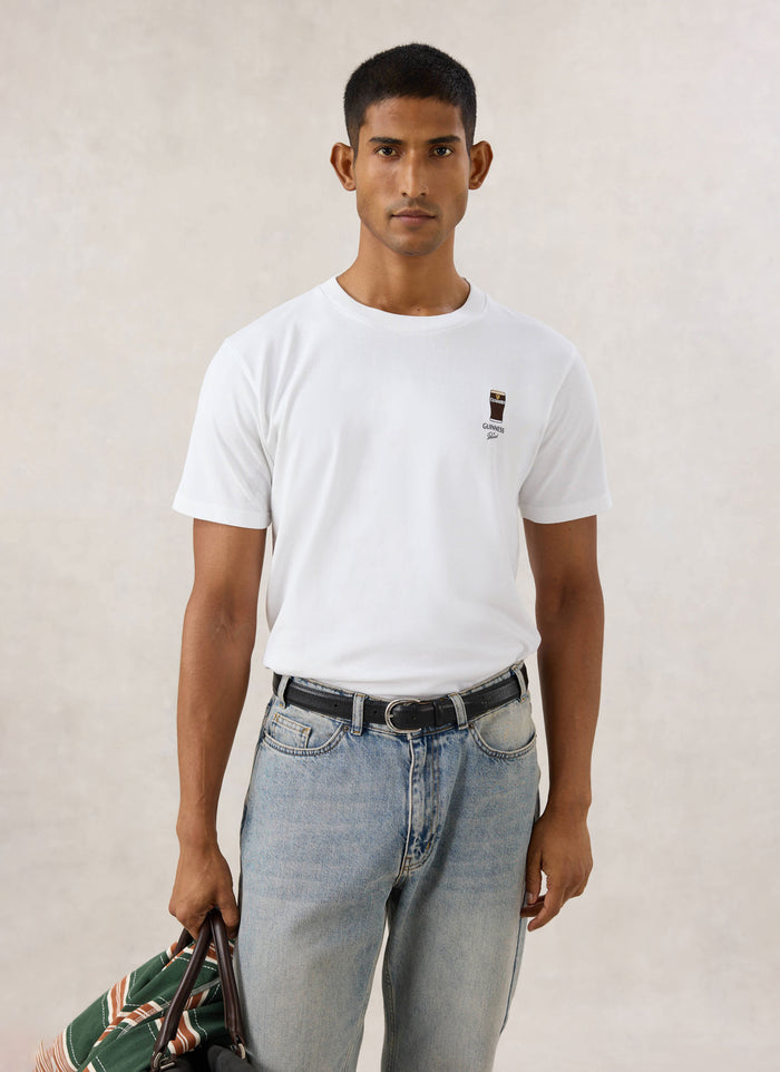Model wearing the white Guinness x Percival stout embroidered organic cotton t-shirt with blue jeans.