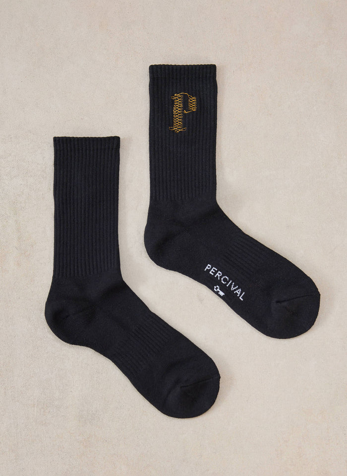 Black Percival Tucker embroidered crew socks in a flat lay, featuring a ribbed cotton blend and gold embroidered P detail.