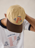 A close-up of a model wearing the tan Percival Tucker soft trucker cap, highlighting the embroidered design.