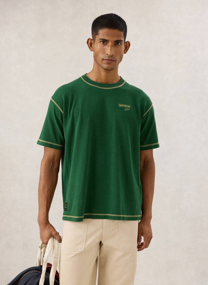 Model wearing the forest green Guinness x Percival oversized T-shirt, showing chest embroidery and contrast stitching.