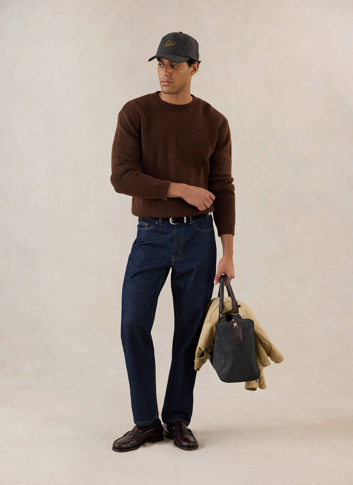 A model wears the espresso Percival mohair jumper with dark denim jeans, loafers, a cap, and a bag in a studio setting.