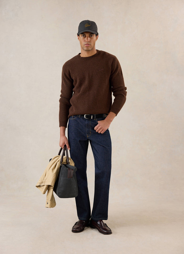 A model wears the espresso Percival mohair boxy crew neck jumper with dark denim jeans, loafers, and a cap.